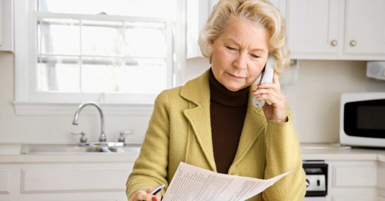 senior woman looking at paperwork and using phone at kitchen island